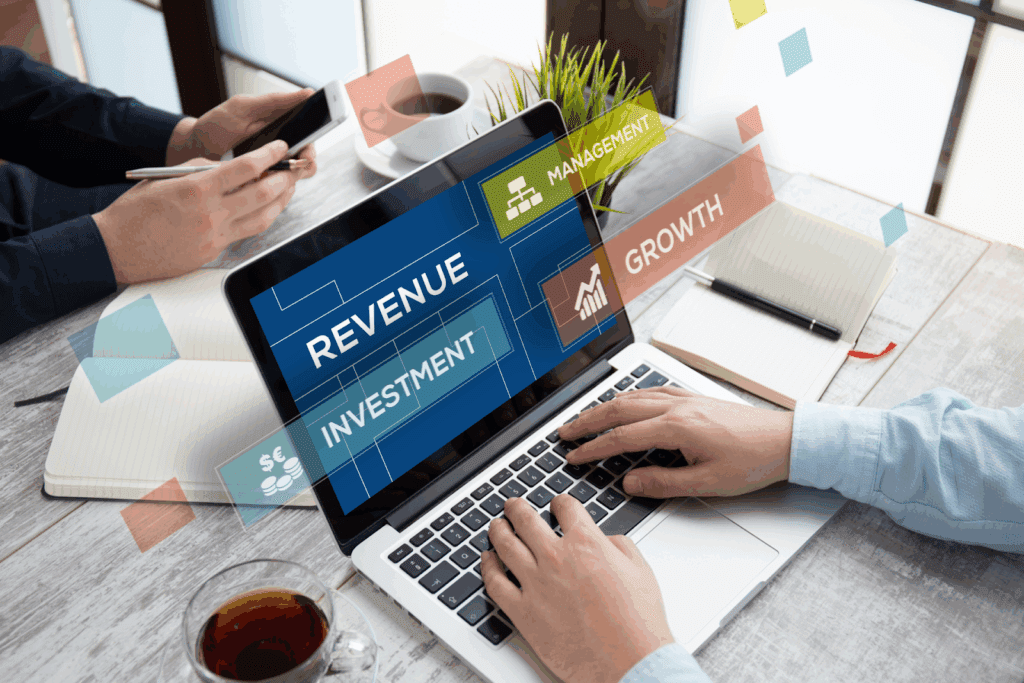 A laptop screen displaying words like Revenue, Investment, Growth, and Management, with digital overlays, while someone types.