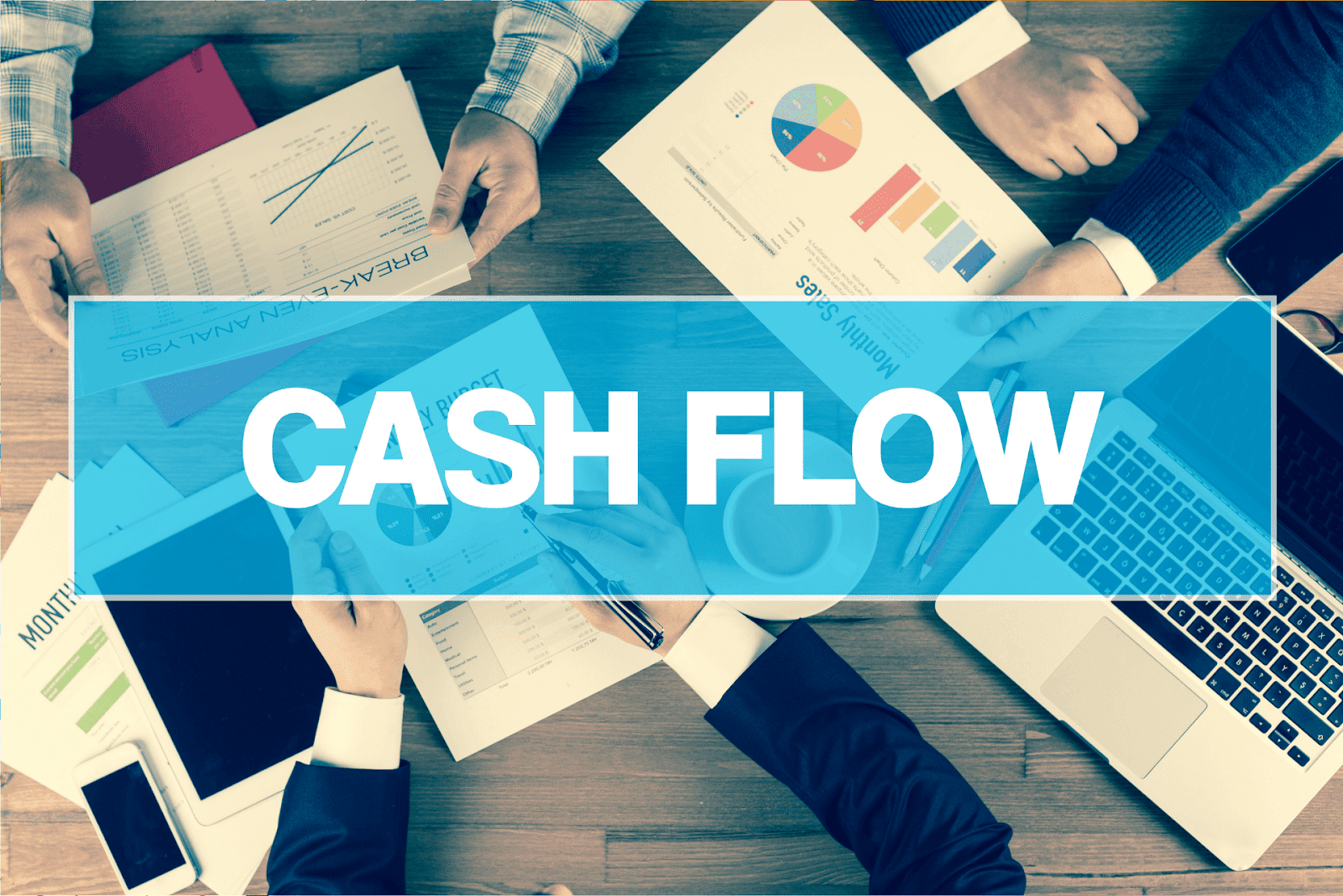 People Reviewing Financial Reports and Charts at a Table with Cash Flow Highlighted in Bold Across the Image People reviewing financial reports and charts at a table with CASH FLOW highlighted in bold across the image