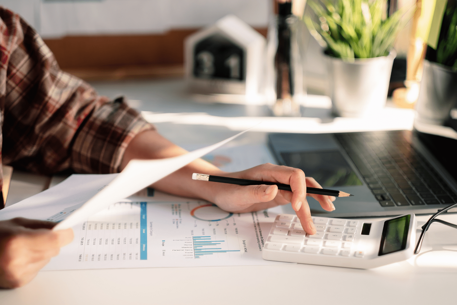 Person Analyzing Financial Charts with a Calculator and Laptop on Desk Person analyzing financial charts with a calculator and laptop on desk