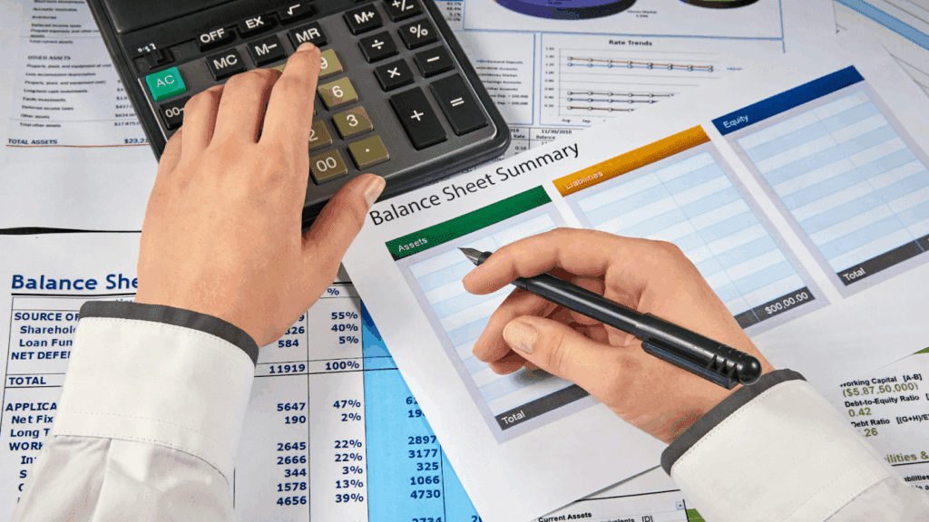 Person reviewing a balance sheet summary with a calculator and pen
