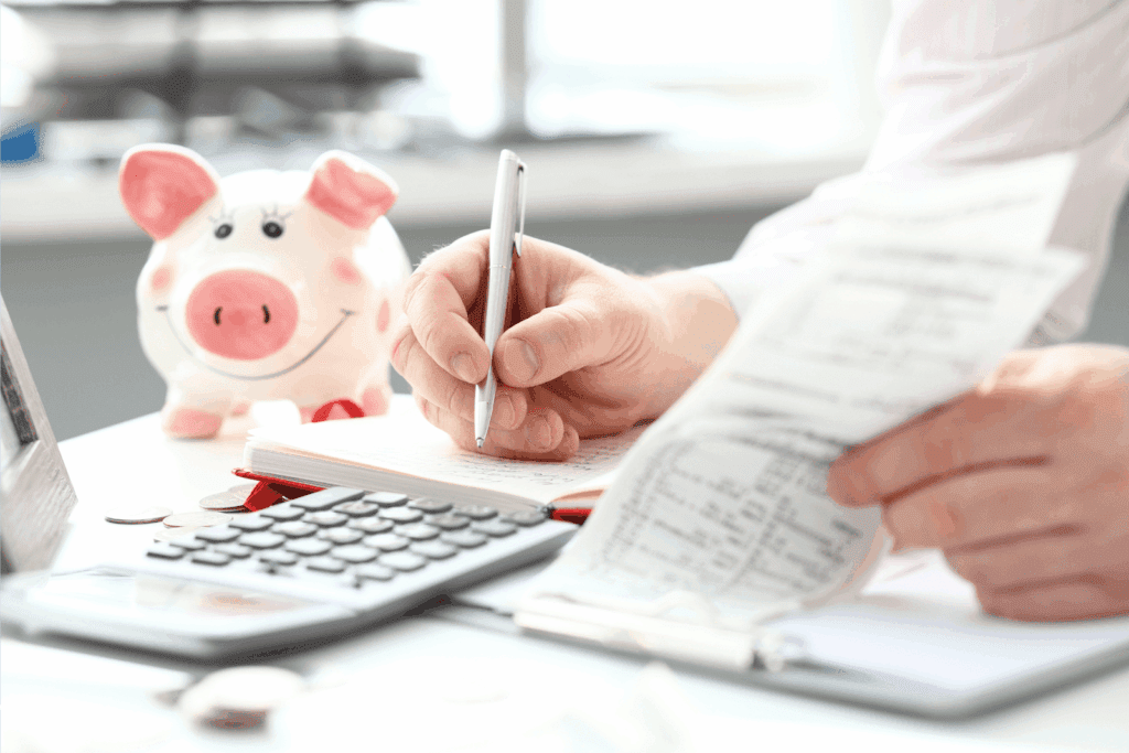 Person reviewing receipts and writing in a notebook with a piggy bank and calculator on the desk