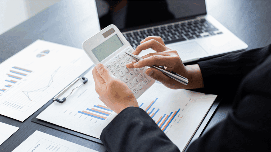 Person using a calculator with financial charts and a laptop