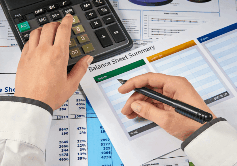 Person reviewing a balance sheet summary with a calculator and pen