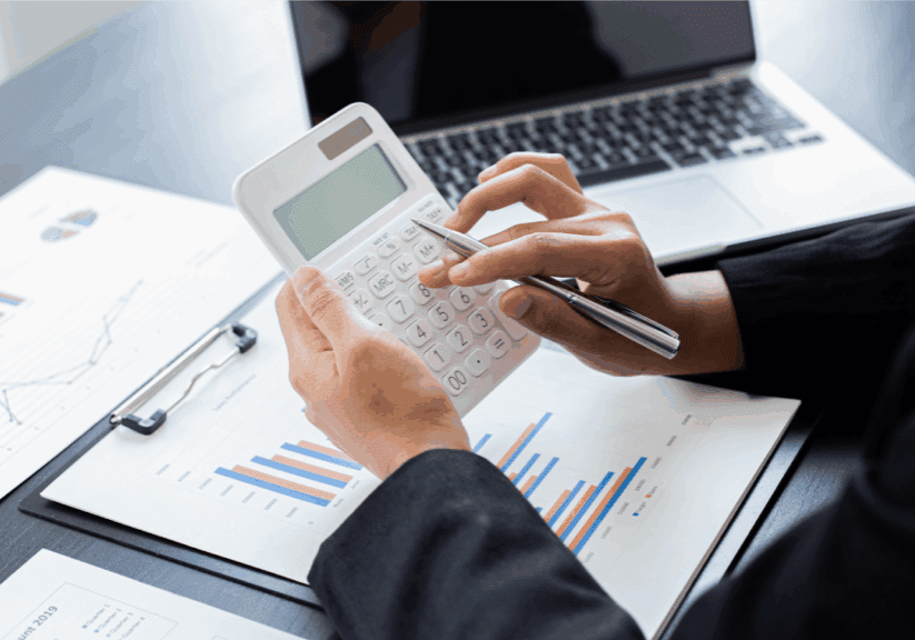 Person using a calculator with financial charts and a laptop