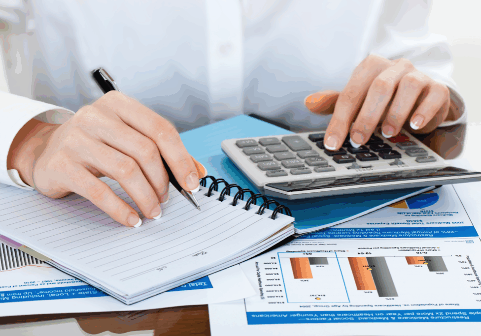 Person writing and using a calculator with financial charts