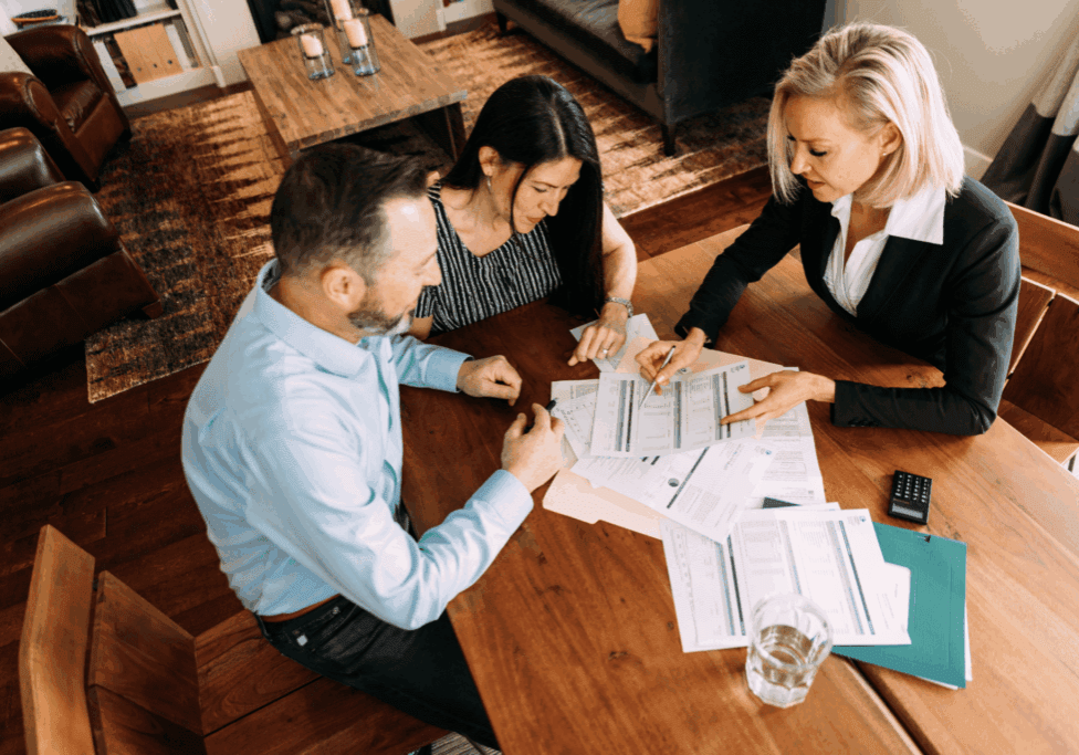 Three people sit around a table in a home-like setting, reviewing financial documents together for a professional financial consultation.