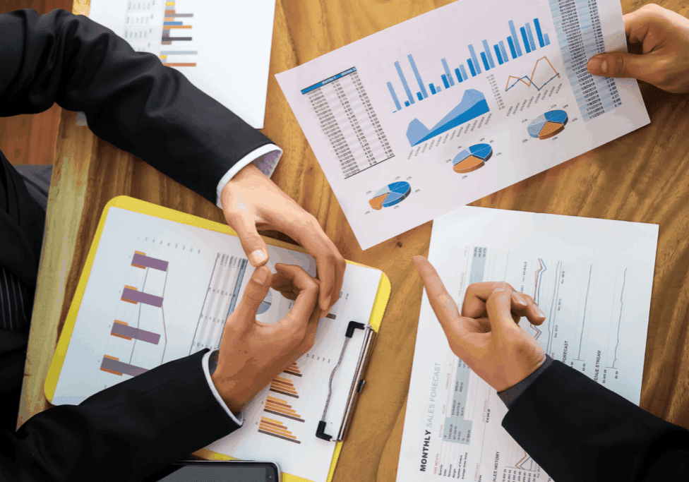Close-up of hands analyzing printed sales reports with bar and pie charts during