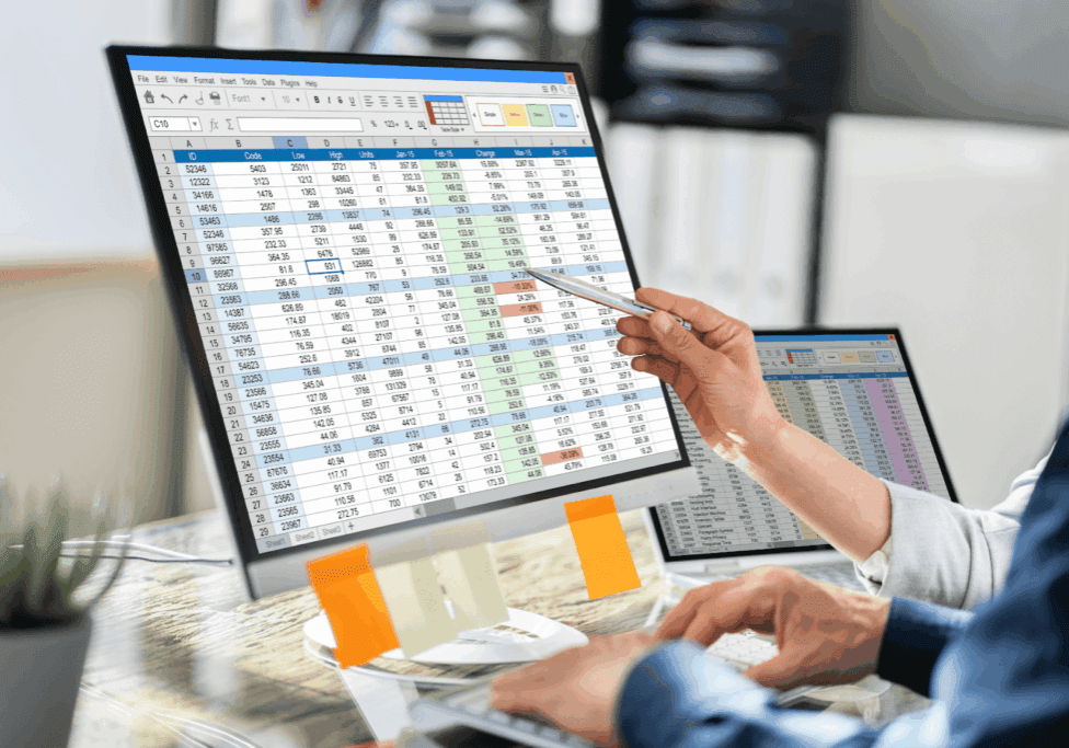 Two people analyzing data on computer screens with spreadsheets.