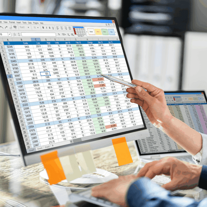 Two people analyzing data on computer screens with spreadsheets.